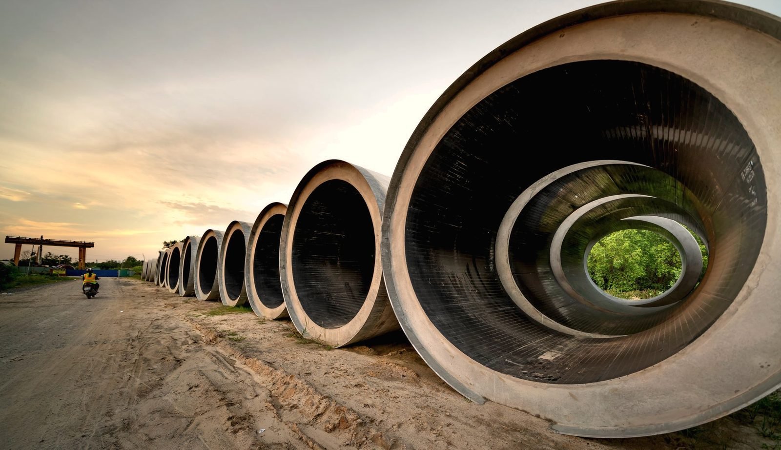 Large concrete pipe sections stacked by a road at sunset