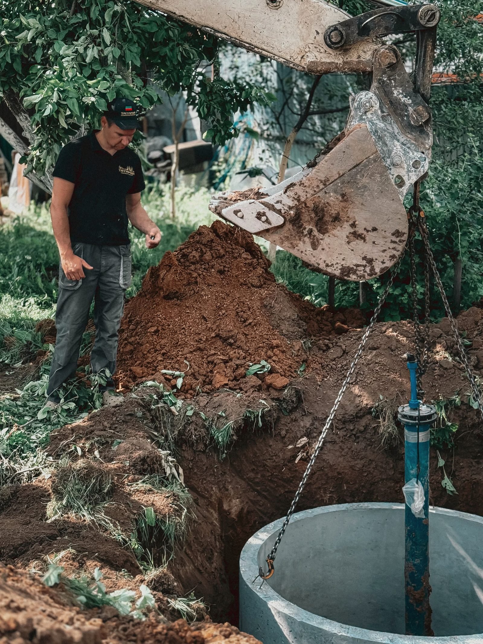 An excavator bucket lowering earth beside a concrete chamber in a hole