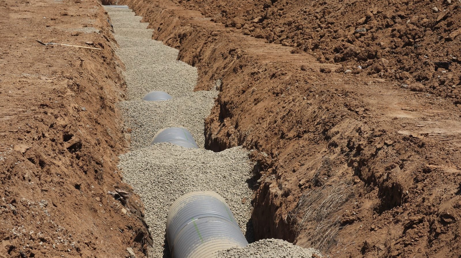 An open drain field trench lined with washed gravel and a length of perforated pipe