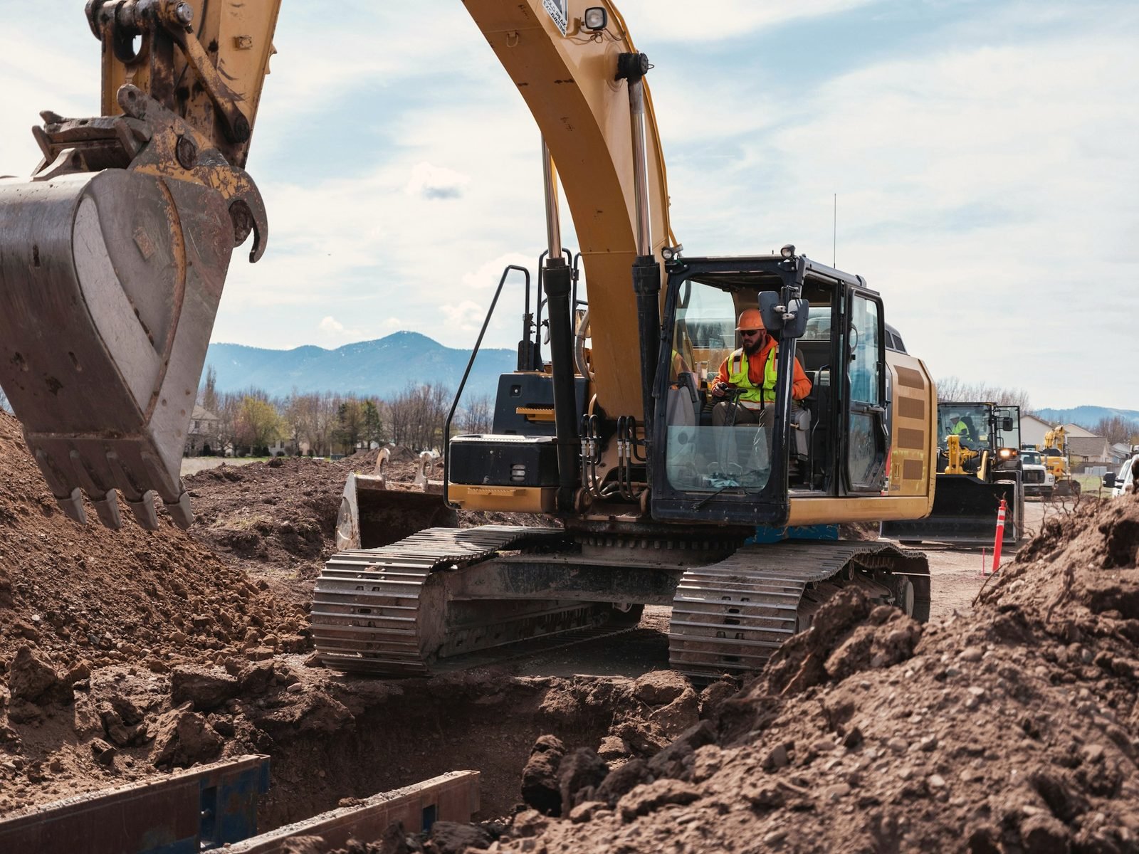 An excavator digging into a deep cut of brown soil
