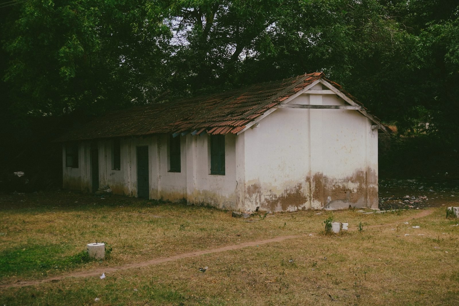 A small white house with a low roof among trees and dry grass