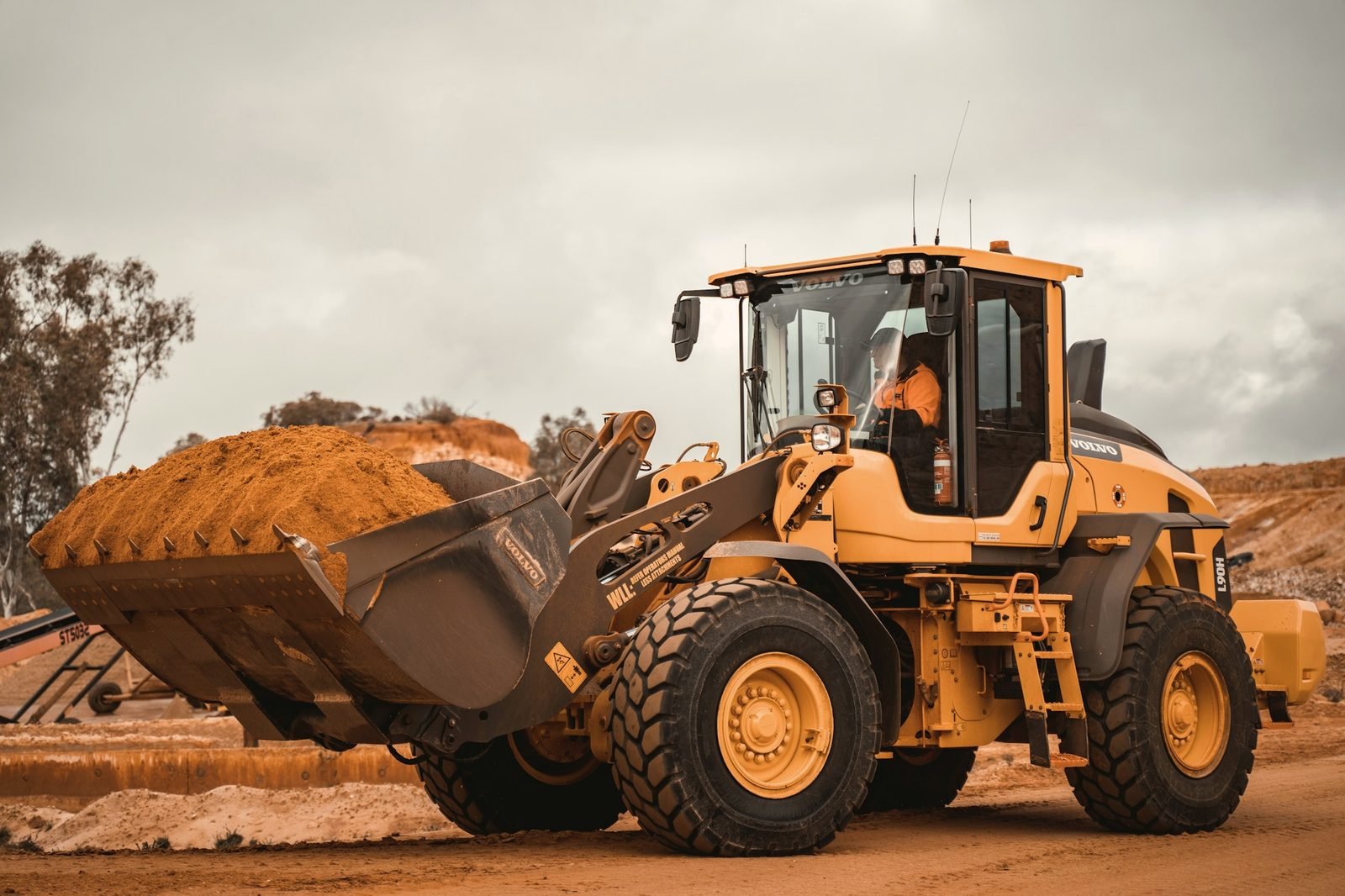 A wheel loader carrying a bucket of orange sand