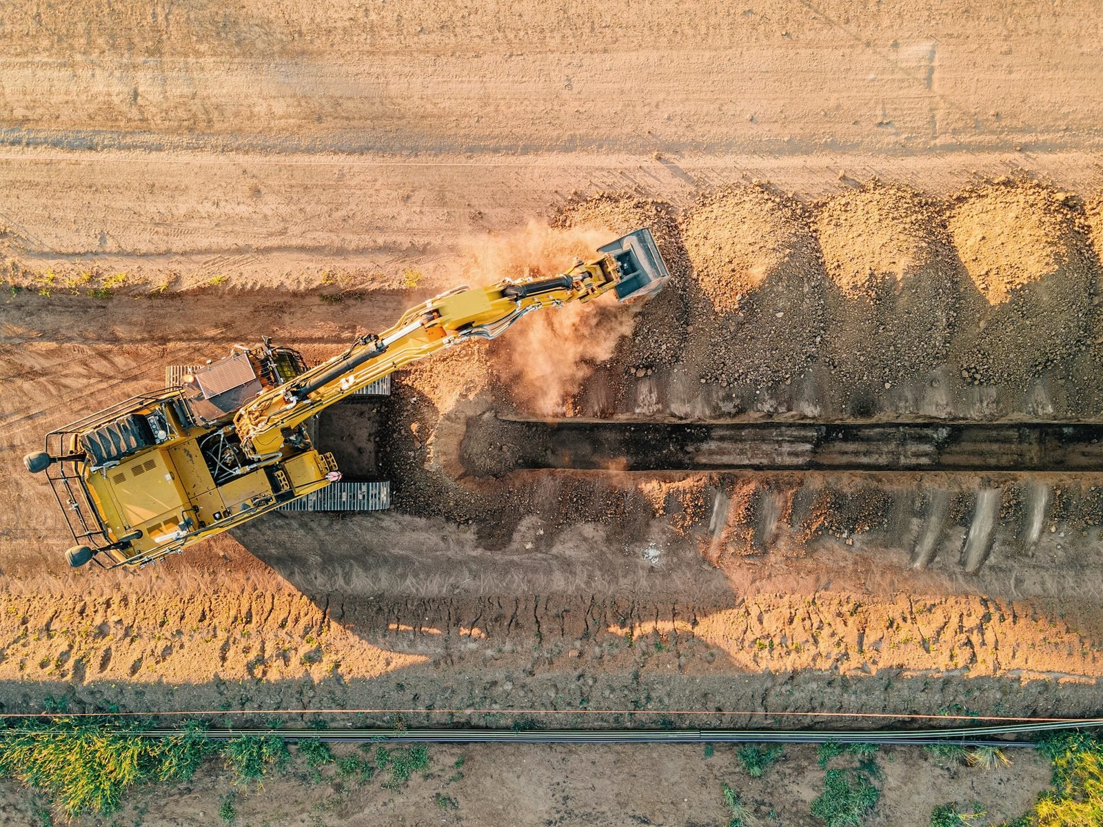 Aerial view of a machine cutting a long trench through sandy ground